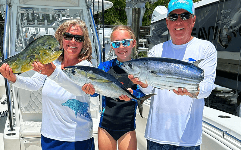 Three anglers holding mahi-mahi and tuna after an offshore fishing charter in Islamorada, Florida Keys.