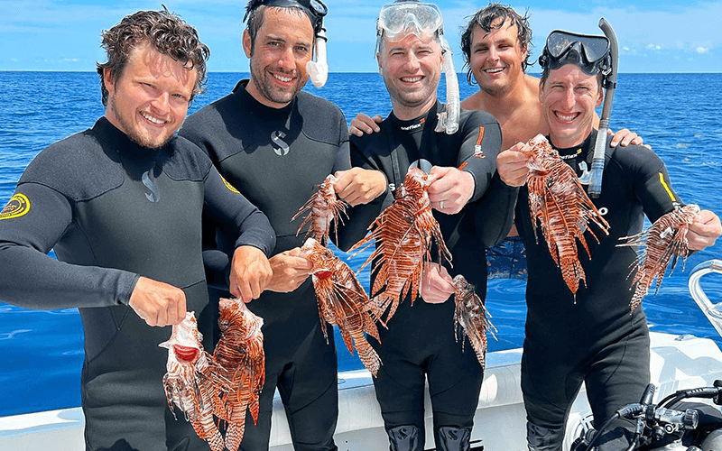 Five scuba divers hold lionfish after diving in Islamorada waters.