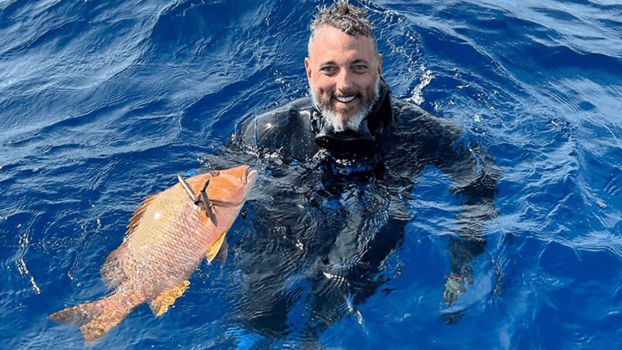 Spearfishing diver holding a freshly caught fish in open blue water.